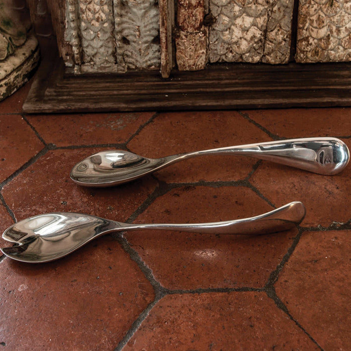 Beatriz Ball Soho twisted serving set in polished aluminum alloy on a rustic tile surface.