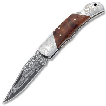 Boker Magnum Damascus Duke folding knife with a patterned steel blade, burl wood handle, and engraved metal bolsters.