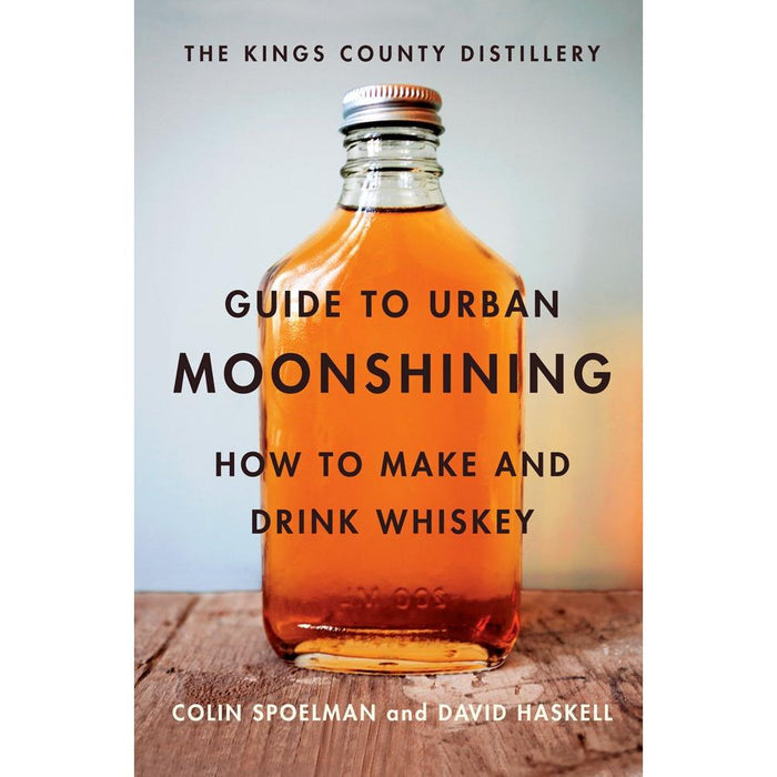 Hardcover book titled Guide to Urban Moonshining featuring a glass bottle of amber whiskey on a rustic wooden surface.