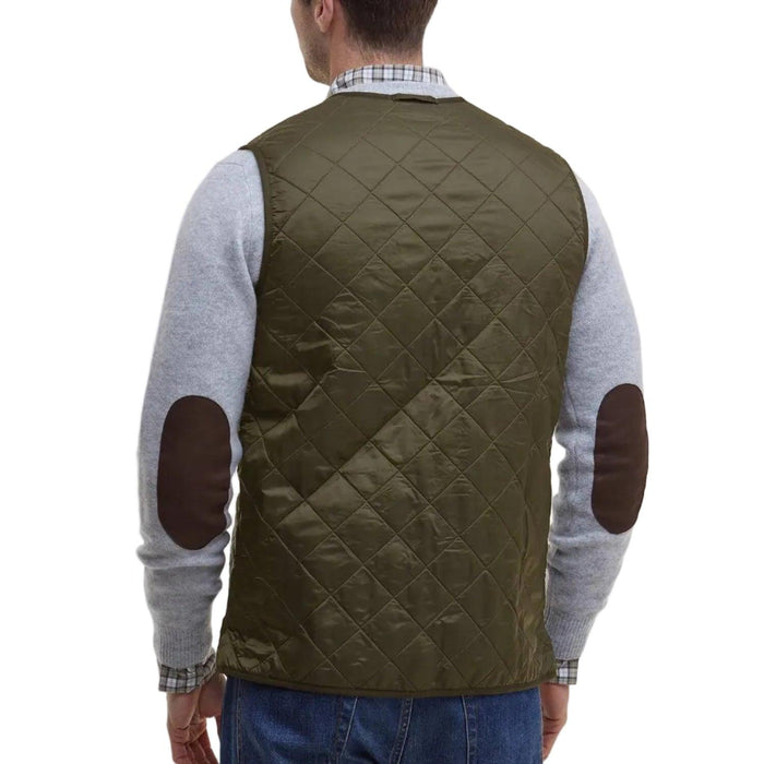 Olive green diamond-quilted Barbour Polarquilt vest worn over a grey sweater with brown elbow patches.