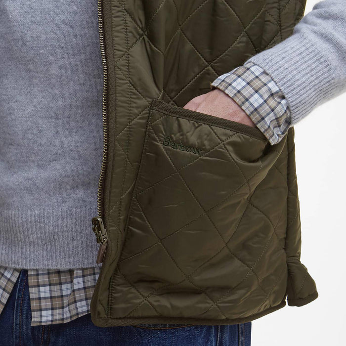 Olive green Barbour diamond-quilted nylon vest with a patch pocket and zip-front closure worn over a sweater.