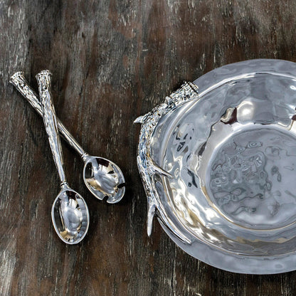 Beatriz Ball silver aluminum salad servers with rustic antler handles next to a matching hammered metal bowl on wood.