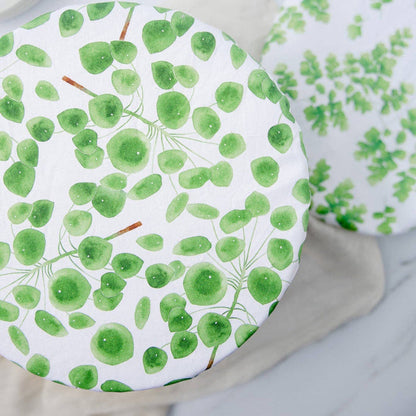 A round white plate or tray with a green watercolor leaf pattern, shown on a light neutral surface with another matching patterned item partially visible in the background.