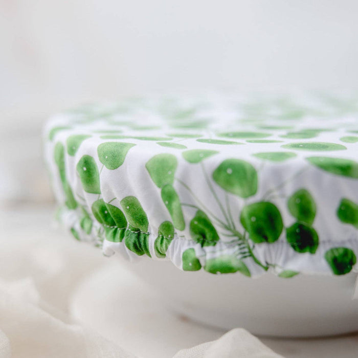 A close-up of a white fabric cover with a green leaf pattern stretched over a round container, set against a soft, light background.