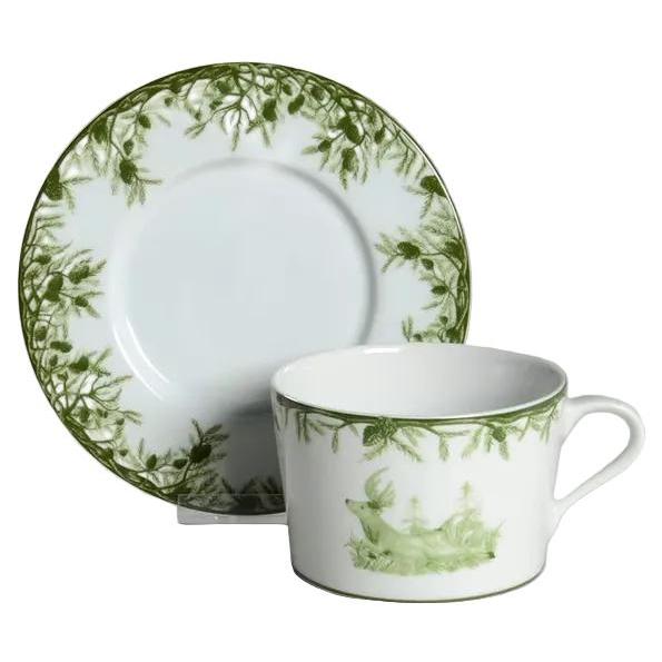 Porcelain 11 oz cup and saucer featuring a green deer and forest pine motif on a white background.