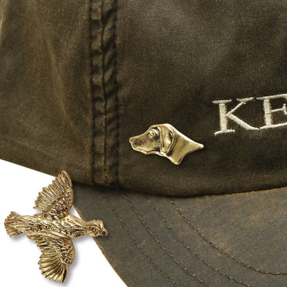 Brass-plated Labrador and quail hunting hat pins attached to a dark olive waxed canvas cap.