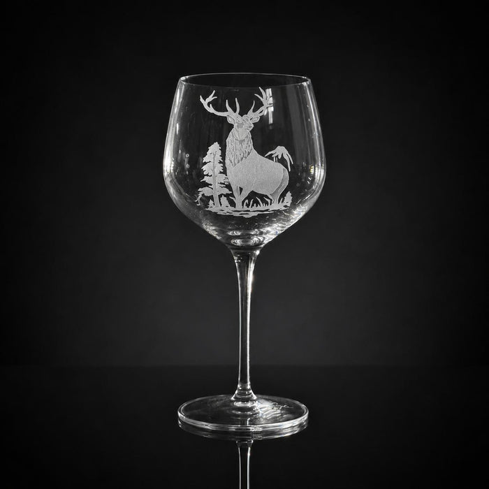 18 oz crystal red wine glass featuring a detailed, hand-carved elk and forest motif against a black background.