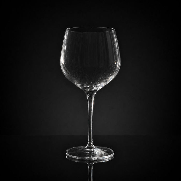 18 oz clear crystal red wine glass with a slender stem, isolated against a dark background.