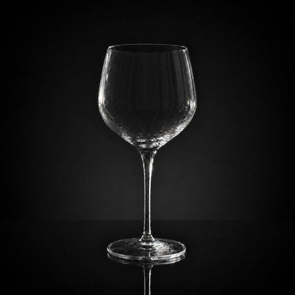 18 oz clear crystal red wine glass with a slender stem, isolated against a dark background.