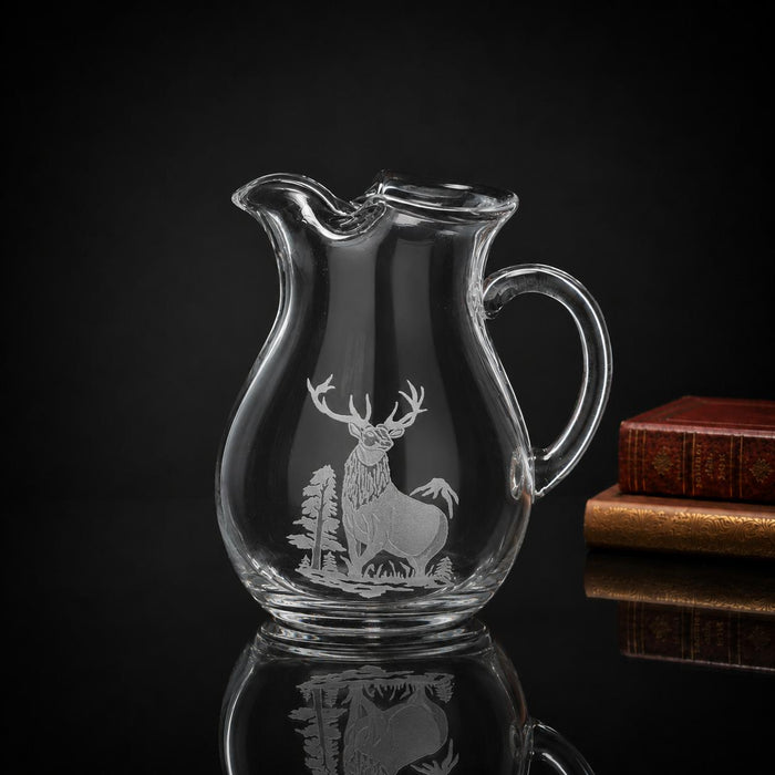 84 oz clear crystal pitcher featuring a multi-layered hand-carved elk and forest design against a dark background.