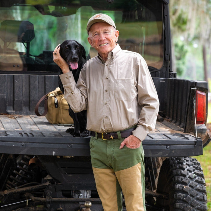 Man wearing a tan long-sleeve Egyptian cotton poplin shirt with a button-down collar, standing by a truck with a black dog.