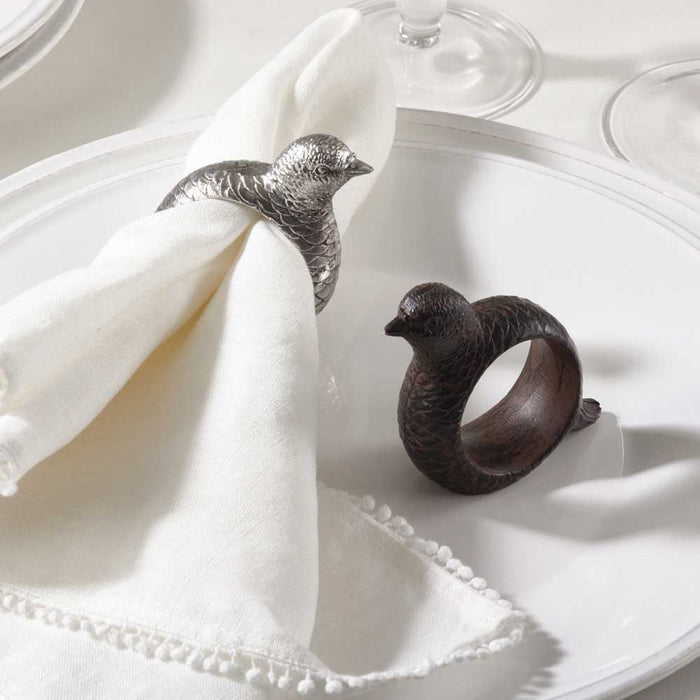 Hand-carved resin pheasant and quail napkin rings in silver and dark brown finishes on a white dinner plate.