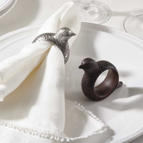Hand-carved resin pheasant and quail napkin rings in silver and dark brown finishes on a white dinner plate.