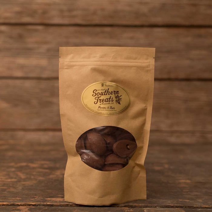 Milk chocolate-covered pecans in a brown stand-up pouch with a Southern Treats label against a rustic wood background.