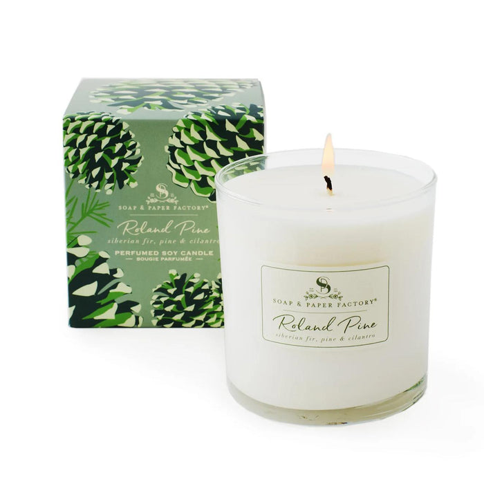 Roland Pine 9.5 oz soy candle in a glass jar with a lit wick next to its green pinecone-patterned box.