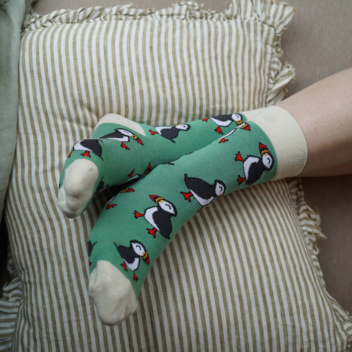 Person wearing green socks with puffin design on a striped cushion