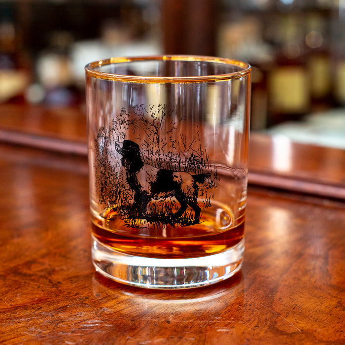 14 oz double old fashioned glass with a gold rim and black etched sporting dog illustration on a wooden bar.
