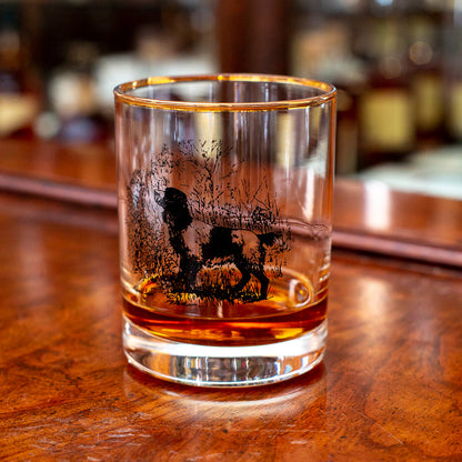 14 oz double old fashioned glass with a gold rim and black etched sporting dog illustration on a wooden bar.
